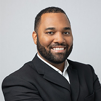 Headshot of a smiling black man in a white shirt with a black suit jacket
