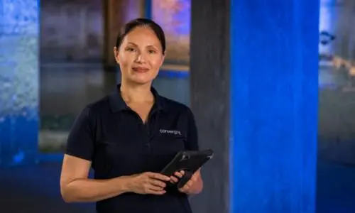 A woman with dark hair and tan skin in a dark blue polo with the Convergint logo on it holding a tablet in her hands