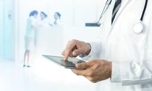 A person in a white doctors coat holding a tablet in their hands