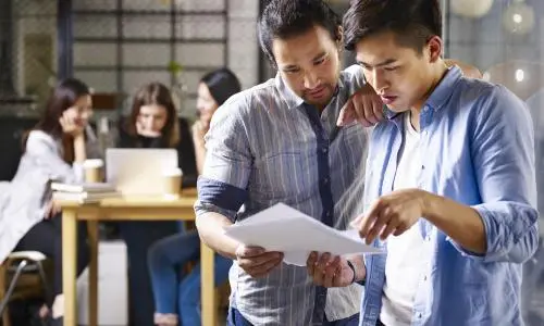Two men standing near each other looking at a piece of paper