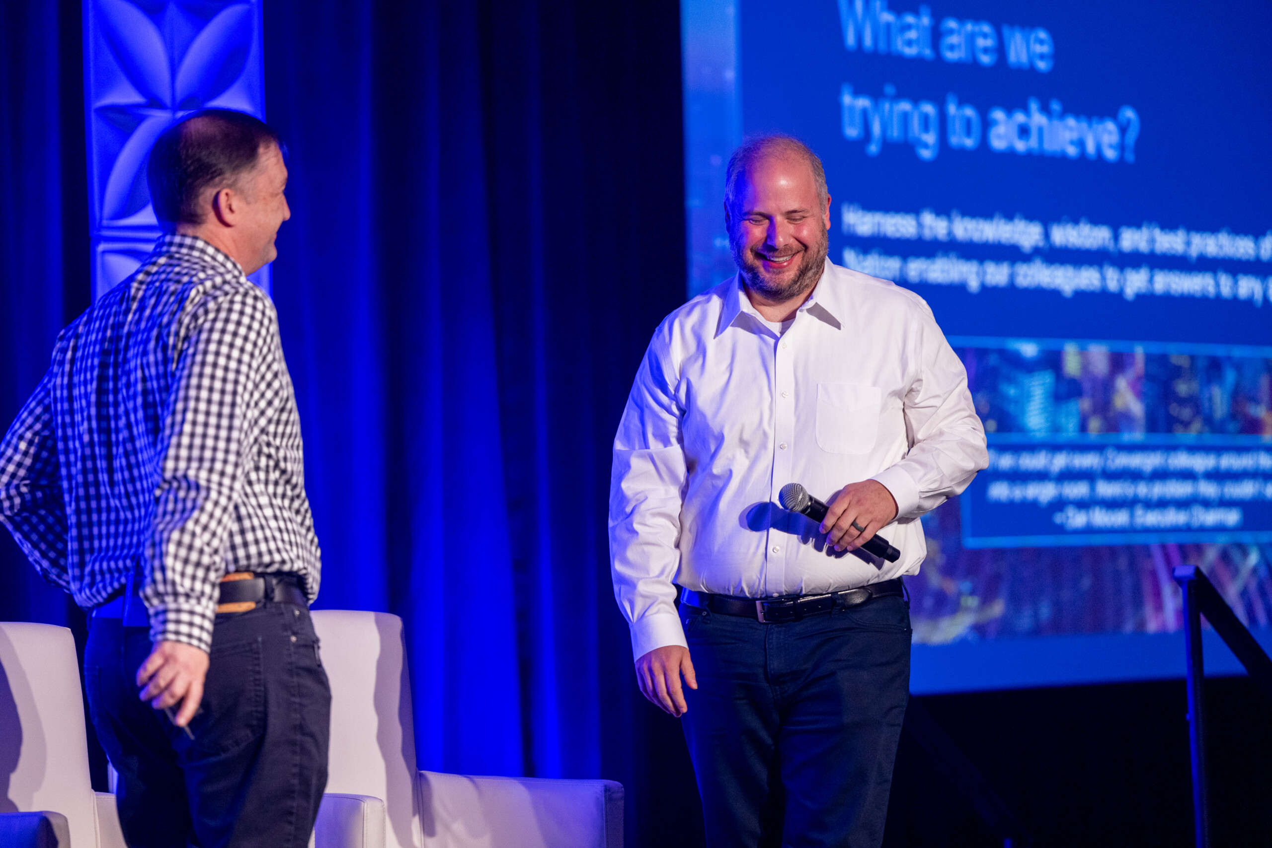 Two men on a stage presenting facing each other and laughing